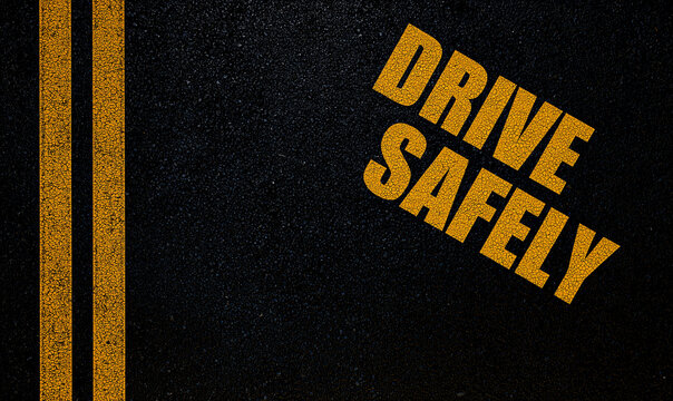 Overhead close up photograph showing a dark textured asphalt road with parallel yellow double lines and the text Drive Safely