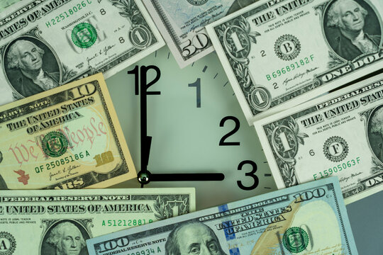 time is money concept showing a close up of an analog clock face surrounded by US dollar bills representing financial investment and deadlines