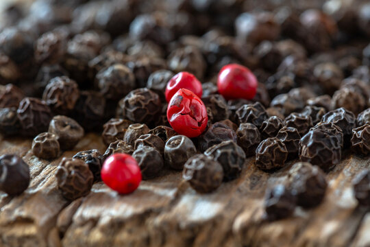 Close-up of black and red peppercorns on rustic wooden surface.