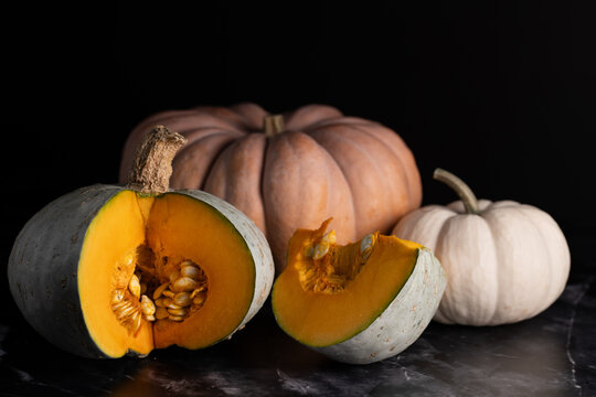 Close-up of various pumpkins against a dark background. One pumpkin has been cut open. The seeds are visible inside.