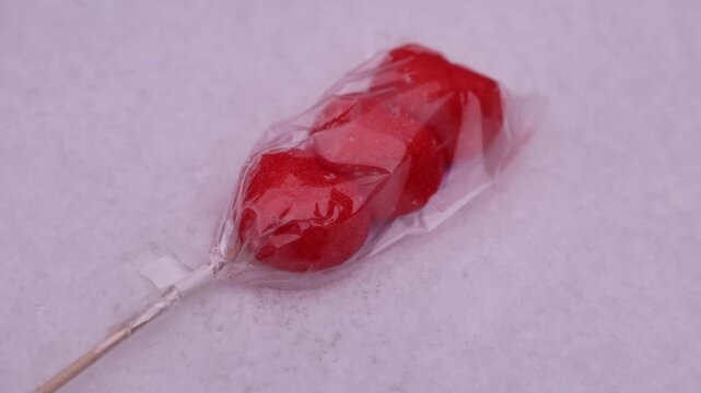 Red fruit candy on stick rotating on pink snowy surface