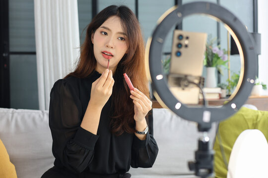 Young Asian influencer filming a beauty makeup tutorial video at home.