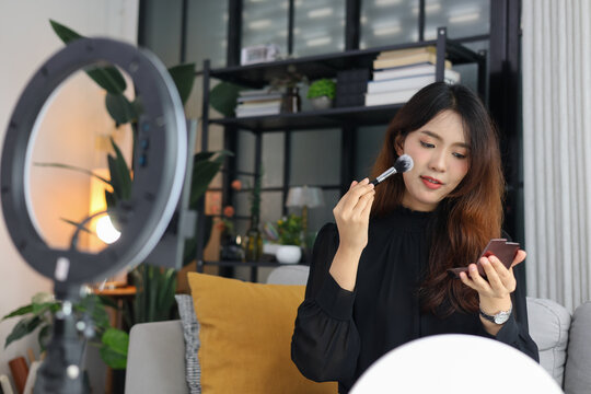 Smiling young woman recording a makeup tutorial blog using a smartphone and ring light.