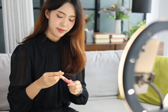 Young Asian influencer filming a beauty makeup tutorial video at home.