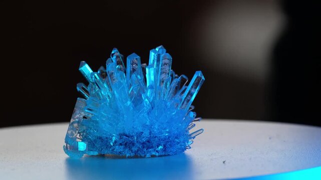 A real crystal. The grown crystal rotates on an illuminated turntable. A scientific experiment and chemical study. A beautiful background or screensaver. Blue.
