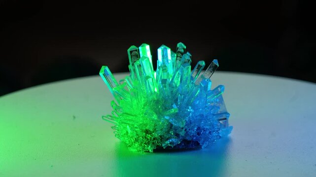 A real crystal. The grown crystal rotates on an illuminated turntable. A scientific experiment and chemical study. A beautiful background or screensaver. Blue and green.