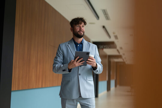 Businessman walking in office hallway holding tablet and coffee