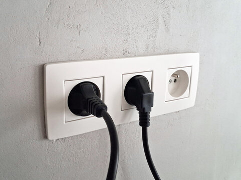Power outlet with two plugs inserted and white empty socket.  Modern socket on interior wall with cables for office or apartment.