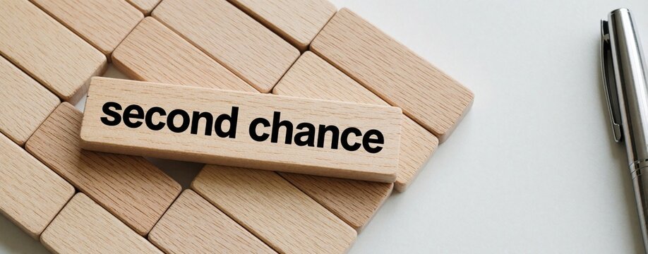 Wooden block with text second chance rests on table near metal pen. Building blocks background suggests opportunity, fresh start, or new beginning. Business decisions.