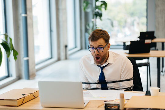 Businessman feeling tied down by office stress looking at laptop