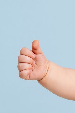 Close-up of a baby hand making a thumbs-up gesture against a clean blue background with copy space