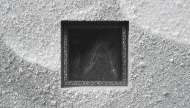 A square window opening in a rough textured gray concrete wall with a dark interior space showing subtle swirling patterns and deep shadows inside