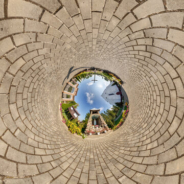 creative tiny planet photo of a rural landscape with dirt road, green fields, and cloudy sky forming a circular world.