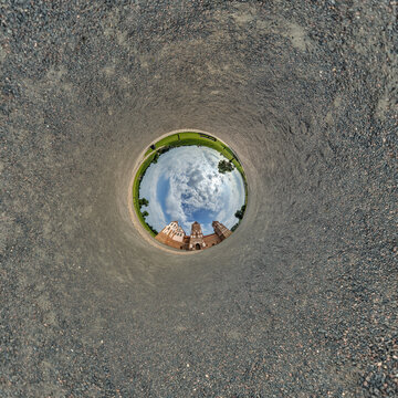 creative tiny planet photo of a rural landscape with dirt road, green fields, and cloudy sky forming a circular world.