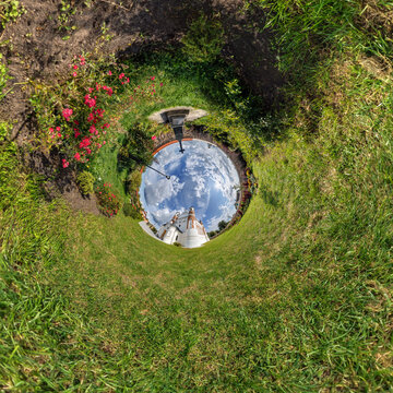 creative tiny planet photo of a rural landscape with dirt road, green fields, and cloudy sky forming a circular world.