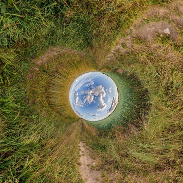 creative tiny planet photo of a rural landscape with dirt road, green fields, and cloudy sky forming a circular world.