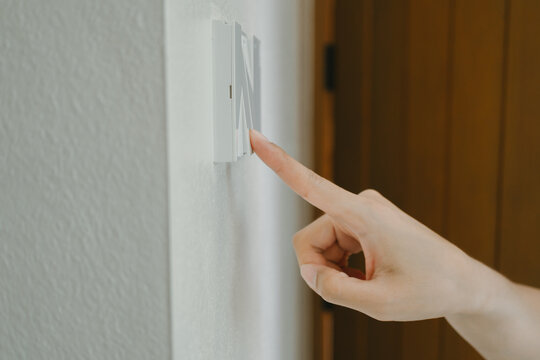 Hand pressing light switch, finger reaching for electric button, calm person toggling wall device, indoor power control, household utility