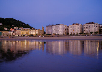 Obraz premium Sunset over Zurriola beach with city reflection on wet sand, San Sebastian, Basque Country, Spain