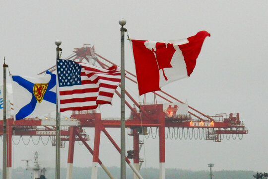 HALIFAX, NS &mdash; JUNE 18, 2018: The flags of Nova Scotia, the United States and Canada fly in front of container cranes at the Halterm terminal in Halifax Harbour.