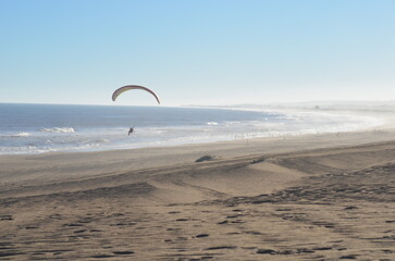 Paramotor pilot flying over the ocean waves and sand dunes at Umlalazi Nature Reserve, South Africa © Michael