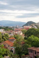 Summer panoramic view of Plovdiv, Bulgaria, from Nebet Tepe, featuring the Metropolitan Church of St. Marina in the foreground, historic red-tiled rooftops, lush greenery, rocky hills and the Rhodope  © snatalia