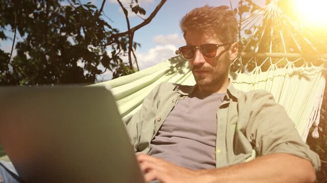 A man is sitting on a hammock with a laptop in front of him