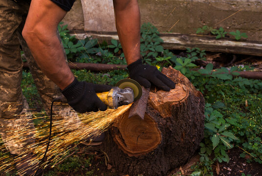 Man in protective gloves cutting metal with an angle grinder outdoors, bright sparks flying. Concept of manual labour, home workshop, DIY metalwork and work safety.