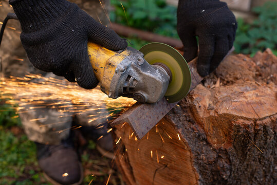 Man in protective gloves cutting metal with an angle grinder outdoors, bright sparks flying. Concept of manual labour, home workshop, DIY metalwork and work safety.