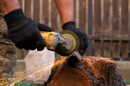 Man in protective gloves cutting metal with an angle grinder outdoors, bright sparks flying. Concept of manual labour, home workshop, DIY metalwork and work safety.