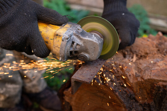 Man in protective gloves cutting metal with an angle grinder outdoors, bright sparks flying. Concept of manual labour, home workshop, DIY metalwork and work safety.