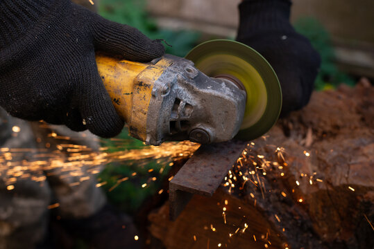 Man in protective gloves cutting metal with an angle grinder outdoors, bright sparks flying. Concept of manual labour, home workshop, DIY metalwork and work safety.