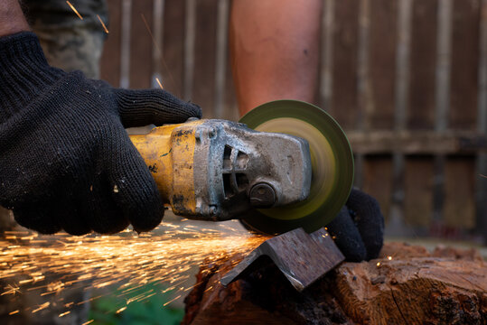 Man in protective gloves cutting metal with an angle grinder outdoors, bright sparks flying. Concept of manual labour, home workshop, DIY metalwork and work safety.