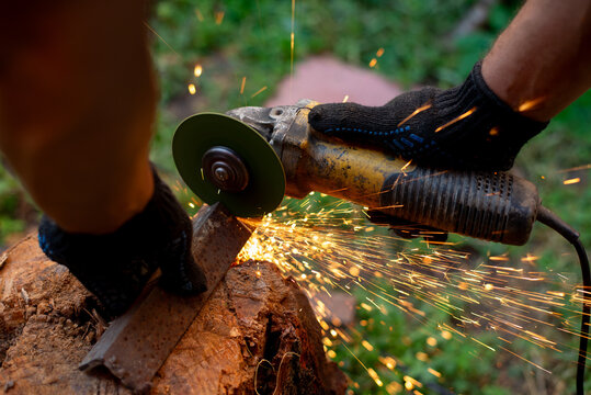 Man in protective gloves cutting metal with an angle grinder outdoors, bright sparks flying. Concept of manual labour, home workshop, DIY metalwork and work safety.