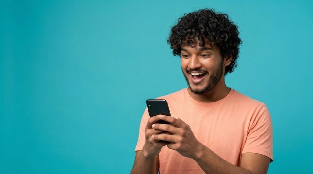 A happy young man with curly hair reacts with a wide smile to his mobile phone screen.