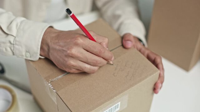 Person marks a cardboard box with a red pencil