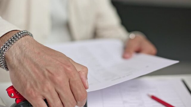 Hands hold papers and a stapler