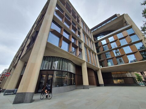 Low angle wide shot of the Bloomberg European Headquarters building in London, showcasing its distinctive modern architecture with bronze angular window fins and large sandy-colored stone structural