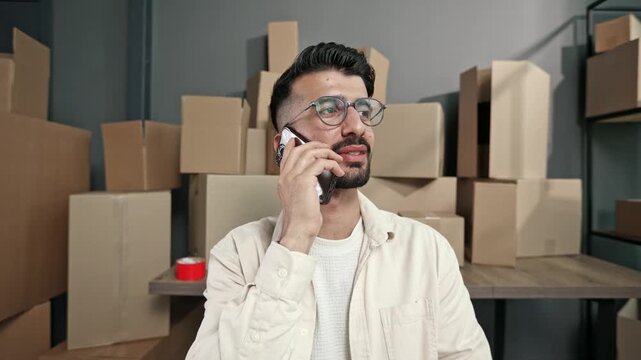 Man speaks on phone amid stacked cardboard boxes