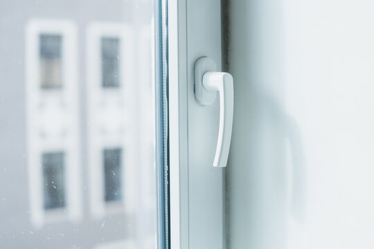 A lever handle sits on a glazed window sash beside its frame and seal, showing the operating hardware used for manual window opening and interior ventilation