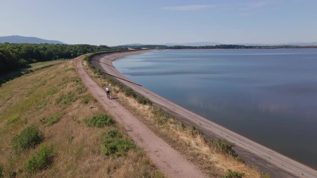Cyclist riding gravel bike along road near large lake, aerial view
