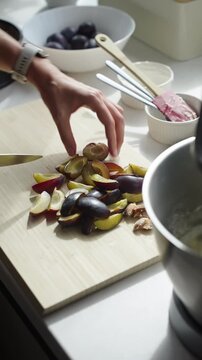 Person cutting fresh plums on a wooden board for making plum pie in the kitchen