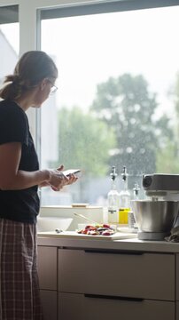 Woman checking recipe on smartphone while cooking in kitchen