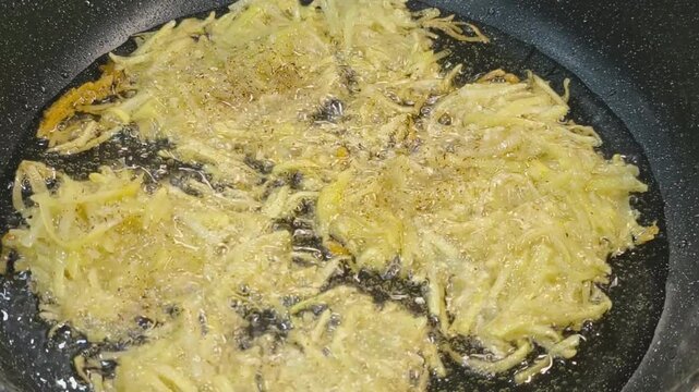 Large grated potato fritter cooking in a frying pan. Hot oil bubbles around the potato pancake as a golden crispy crust forms during frying. Homemade potato pancake made from coarsely grated potatoes.