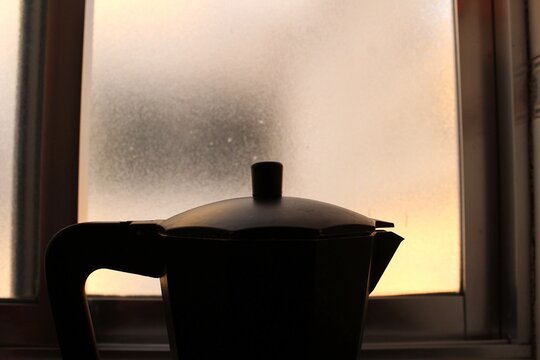 Silueta de cafetera italiana a contraluz frente a una ventana al atardecer