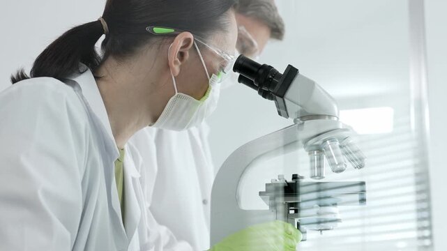 Researchers actively performing scientific analysis in a laboratory. Looking through a microscope to examine biological samples. Focusing on discovery. Innovation