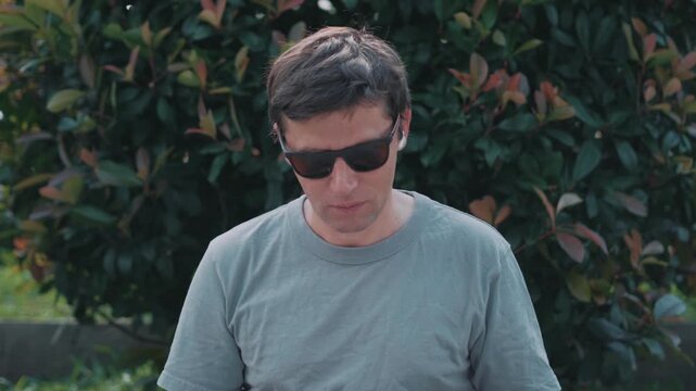 Man using wireless earbuds with noise cancellation in urban park, blocking city noise and enjoying calm listening experience, relaxation and personal audio comfort.