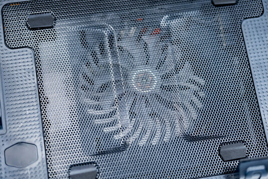 Laptop cooling pad with a large fan beneath perforated metal mesh and supporting pads, providing supplementary airflow for portable computer thermal management