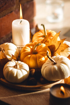 Cozy home decoration on the windowsill with little pumpkins and candles. Aromatherapy for fall season. Aesthetics, seasonal atmospheric vibes. Thanksgiving dinner decor idea.