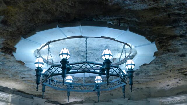 Medieval iron chandelier hanging in a grotto. Elegant and ancient iron chandelier with modern led lights hanging from the rough stone ceiling of a natural cave