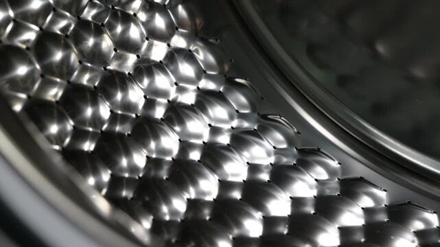 Close-up dolly out from inside washing machine drum. Detailed close-up view moving out from the shiny stainless steel drum of an empty, modern washing machine, revealing the honeycomb pattern